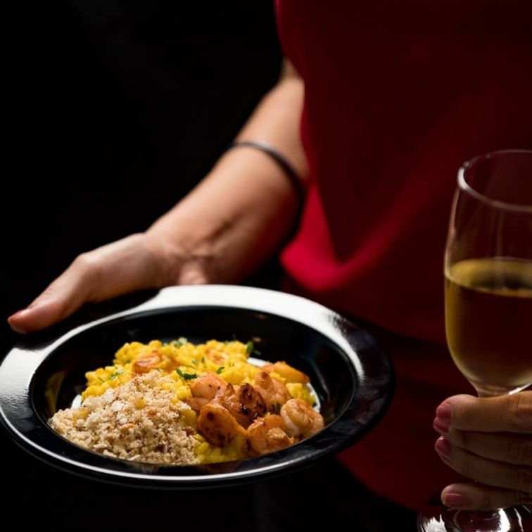 Prato de risoto com camarão sendo servido, com taça de vinho branco